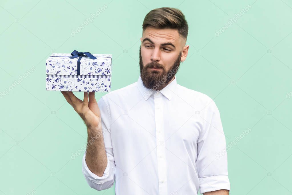 Hmm what is it! Bearded man looking at gift box and want too open. Light green background. Studio shot