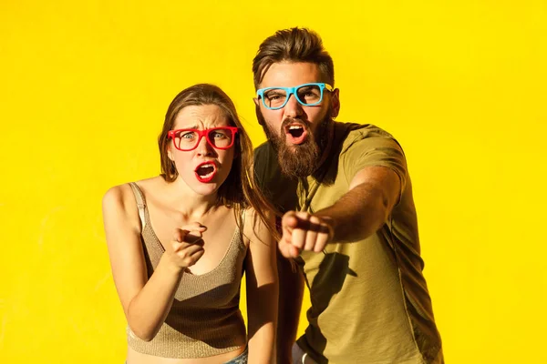 Hej vy! Mladý dospělý vousatý muž a roztomilá brunetka ukazují prstem a při pohledu na fotoaparát. Na žlutém podkladu. Indoor, studio zastřelil — Stock fotografie