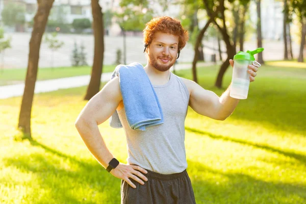 Funny redhead muscular man showing bottle and lookingat camera. Outdoor shot — Stock Photo, Image