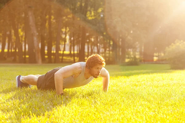 Push-ups. Zonnige. Zomer. Roodharige en bebaarde fitness model doet push ups. Buiten — Stockfoto