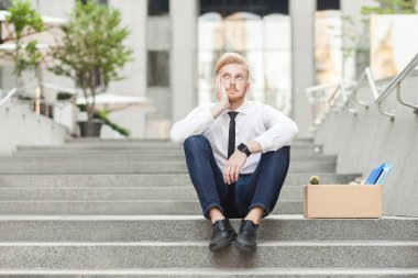 Unfair ginger young adult worker sit on stairs and wondering. clipart