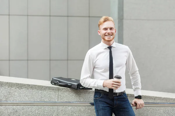 Glück Geschäftsmann mit Tasse, Blick in die Kamera und zahmes Lächeln. — Stockfoto