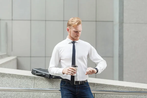 Red haired businessman looking at smart watch and holding cup. — Stock Photo, Image