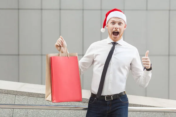 Ung vuxen ingefära affärsman tummen upp och titta på kameran med chockad ansikte. — Stockfoto