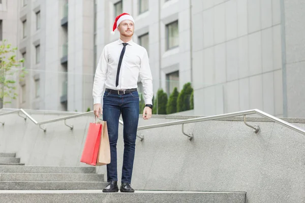 Sucesso jovem adulto gengibre empresário com santa chapéu vermelho, olhando para longe e segurando presentes — Fotografia de Stock