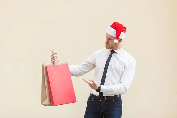 Vendredi noir en hiver. Bonheur homme d'affaires tête rouge en santa chapeau, tenant des sacs à provisions sur les mains, pointant du doigt et regardant les cadeaux . — Photo