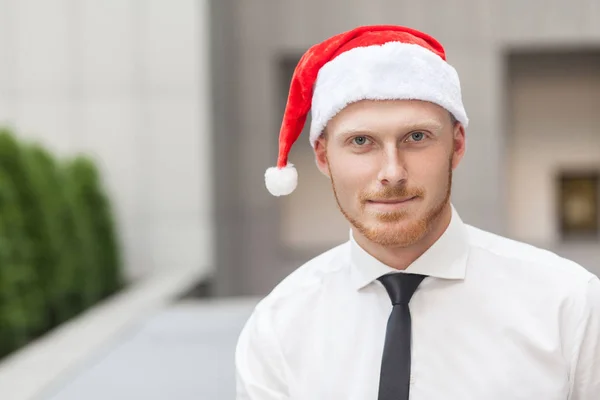 Portret powodzenie czerwony głowa i Brodaty biznesmen na santa hat. Patrząc na kamery i uśmiechając się. — Zdjęcie stockowe