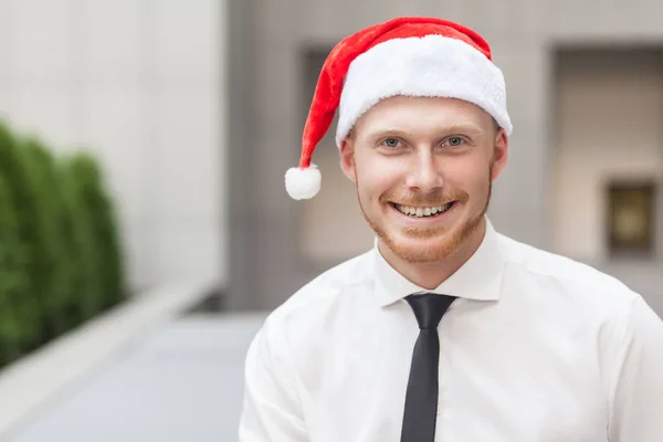 Porträtt av framgång ingefära affärsman på santa hatt. Titta på kameran och toothy leende. — Stockfoto