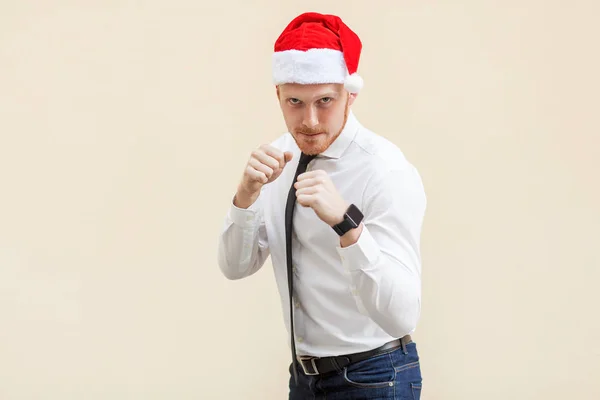 Boxing. Young adult ginger businessman on red santa hat, ready for fight on light orange background. — Stock Photo, Image