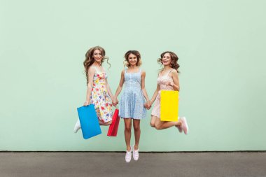 Mutlu güzel üç arkadaş olan renkli paketleri önünde yeşil arka plan alışveriş sonra atlama