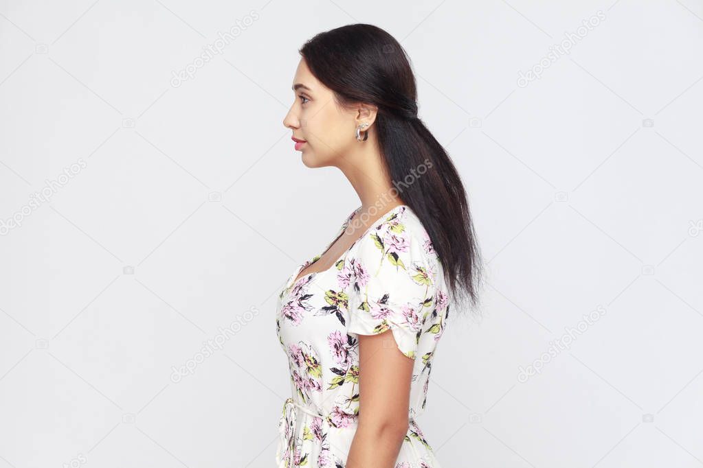 Side view of beautiful young adult woman, standing alone at gray