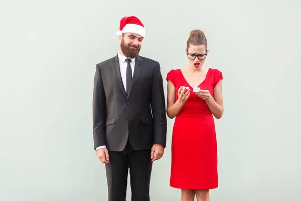 Stolzer Mann mit Weihnachtsmütze auf der Suche nach einem Geschenk. Frustrierte Frau festgehalten — Stockfoto