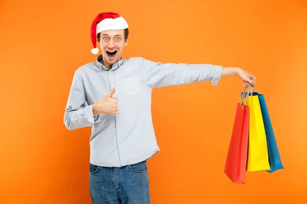 Homem de boné vermelho, segurando muitos sacos coloridos após a loja de natal — Fotografia de Stock