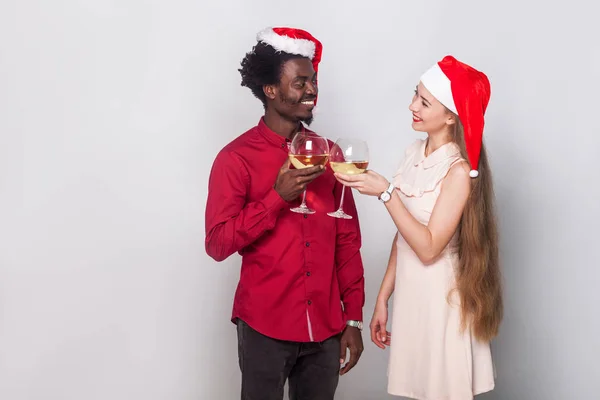 Concept de flirt et d'amour. Homme et jeune femme adulte en bonnet de Noël, tenant des verres de champagne et se regardant avec amour. Plan intérieur — Photo