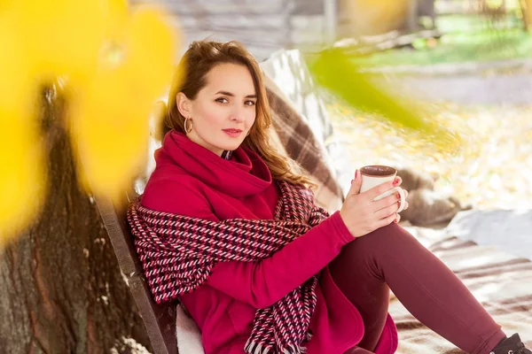 Mulher bonito sentar no banco no parque de outono, segurando copo — Fotografia de Stock