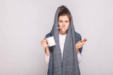 Kupası, termometre ve hapları tutan genç kadın ile gri eşarp,