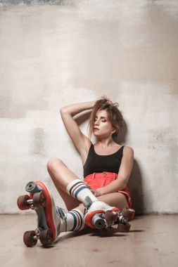 Güzel esmer kız sakin ol, paten yerde oturuyor. Stüdyo çekim, çatı katı iç