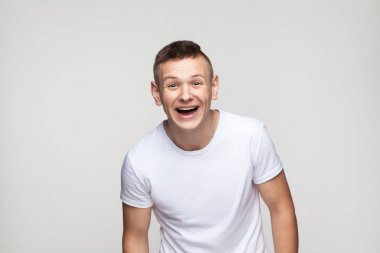 Genç başarı adam kamera ve dişlek gülümseme bakarak. Atış, arka planı gri studio