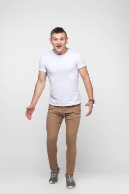 Şok olmuş genç bir adam kameraya bakıyor. İç çekim, gri arkaplan