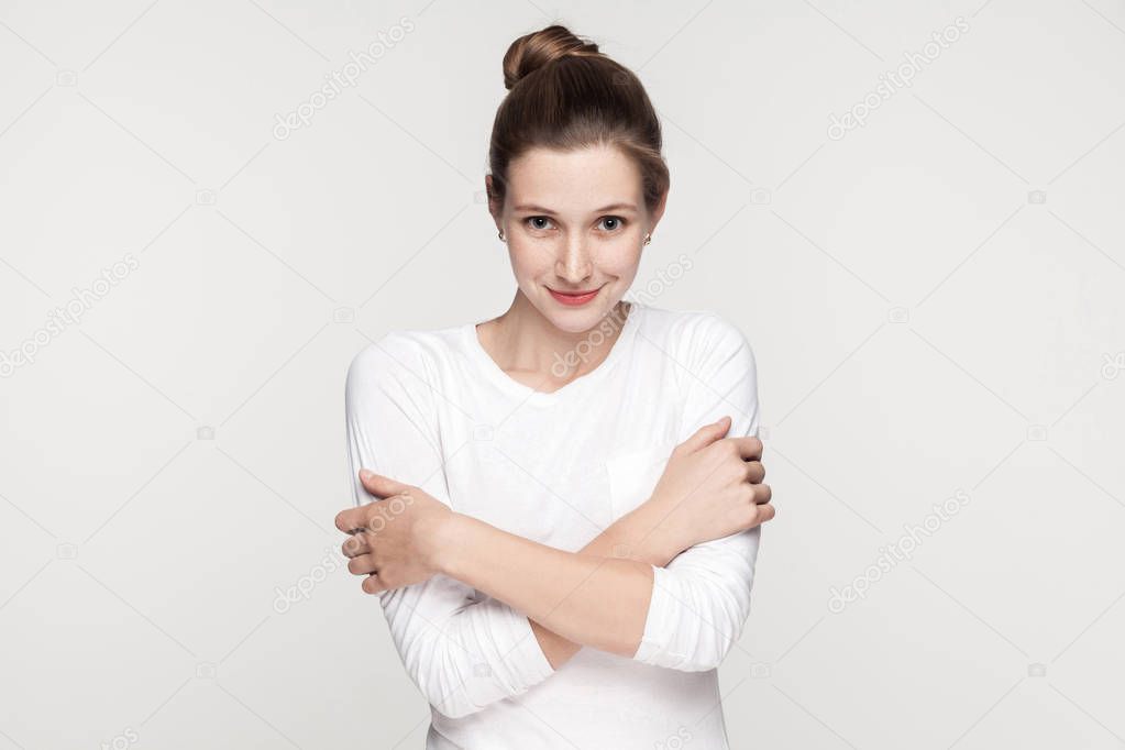 Attractive beautiful freckles woman embrace himself and looking at camera. Studio shot, isolated on gray background