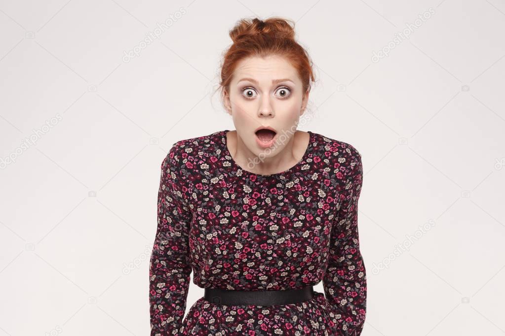 shocked redhead young woman with opened mouth and big eyes looking at camera  