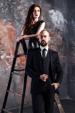 eski püskü duvar arka plan üzerinde yakışıklı işadamı yakınındaki eski bir merdiven üzerinde duran Kızıl saçlı kadın 