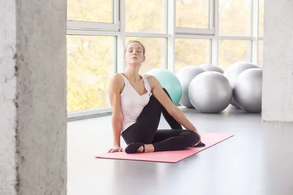 woman with closed eyes doing yoga in cow face posture in gym