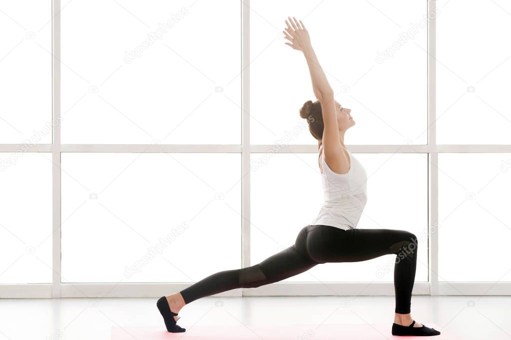 Woman doing yoga while standing in warrior one posture in gym 