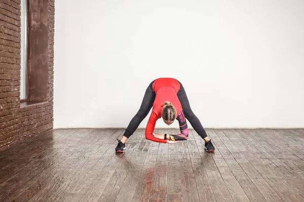 スポーティな金髪女性木質系床の Uttanasana ポーズで立ちながらヨガの練習 — ストック写真