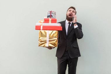 hediye kutuları tutarak ve telefon gri arka plan üzerinde bağıran kızgın işadamı