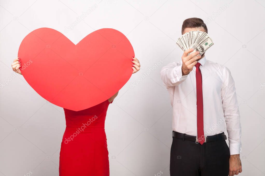 couple holding in hands money and big red heart on gray background, choice concept