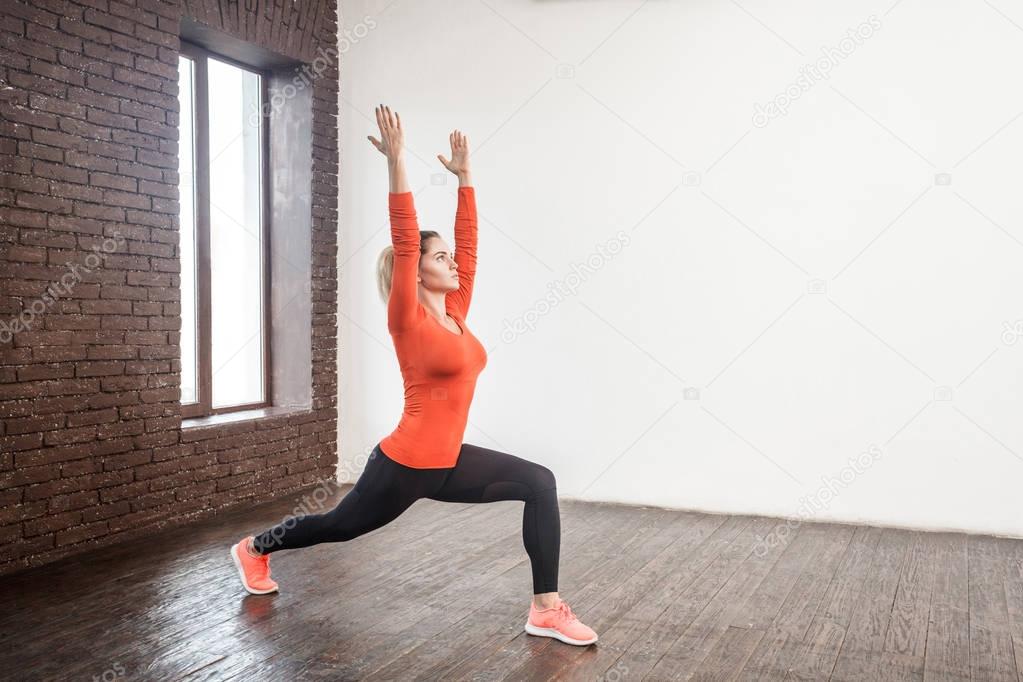 adult woman in sportswear  practicing in stretching and squatting with hands up in front of window
