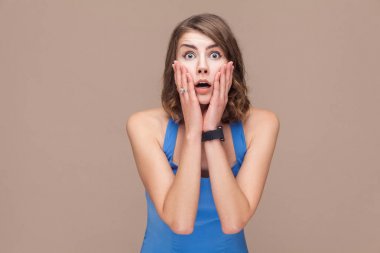 shocked woman with opened mouth looking at camera on light brown background, good new concept