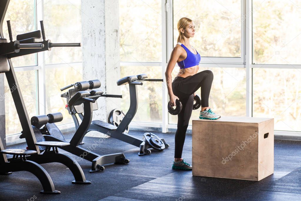 woman with dumbbells doing cross fit exercise on cube 