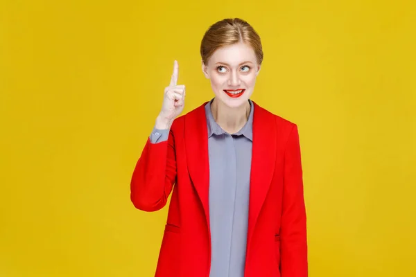 redhead businesswoman in red jacket pointing finger up, idea concept