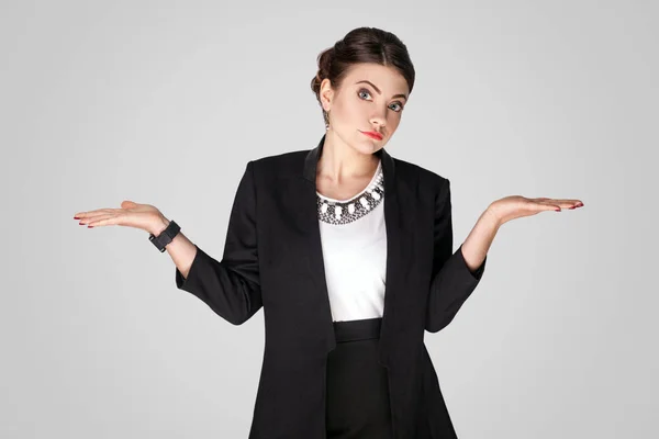 puzzled businesswoman with raised hands posing on grey background