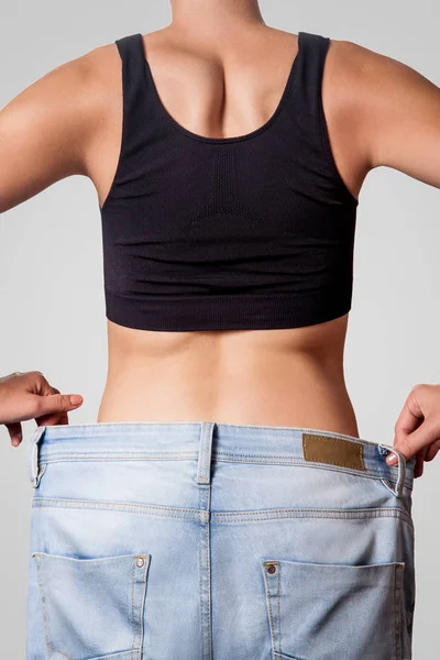 在大牛仔裤的年轻女子苗条的腰部后视图显示成功减肥 饮食观念 — 图库照片