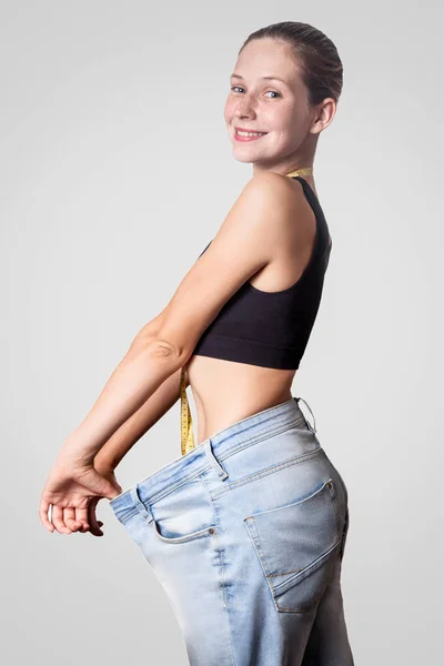 年轻女子苗条腰部的侧面看与测量磁带在脖子在大牛仔裤显示成功的减肥 饮食概念 — 图库照片