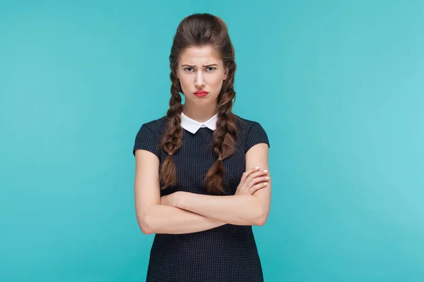 unhappy businesswoman standing with crossed arms and looking at camera with sadness on  blue background