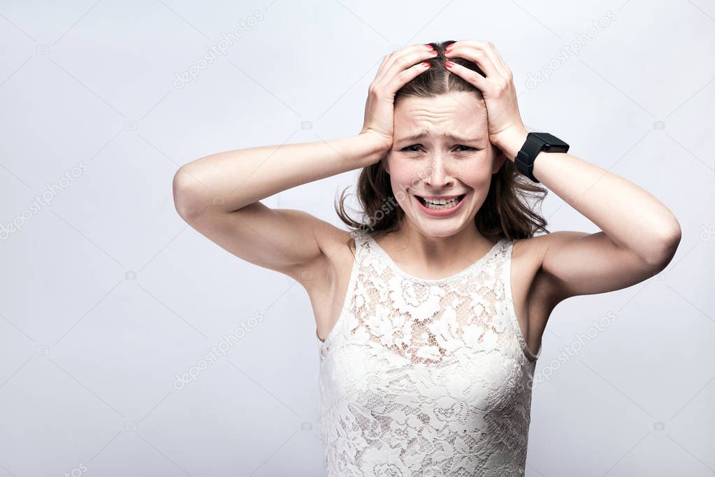 beautiful woman with freckles in white dress with smart watch crying and touching head by hands while having headache, healthcare and medicine concept
