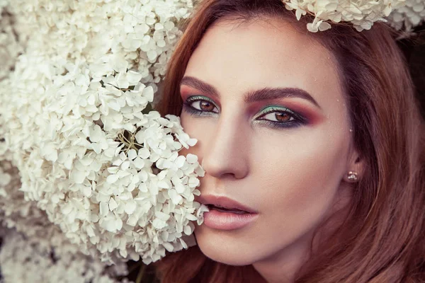 portrait of cute woman with vogue makeup  looking at camera among flowers , summer concept