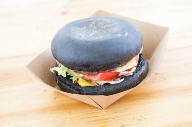 siyah burger sığır eti güveç ve peynir domates ve salata yaprağı üzerinde kağıt kutusu ahşap yüzey üzerinde hizmet 