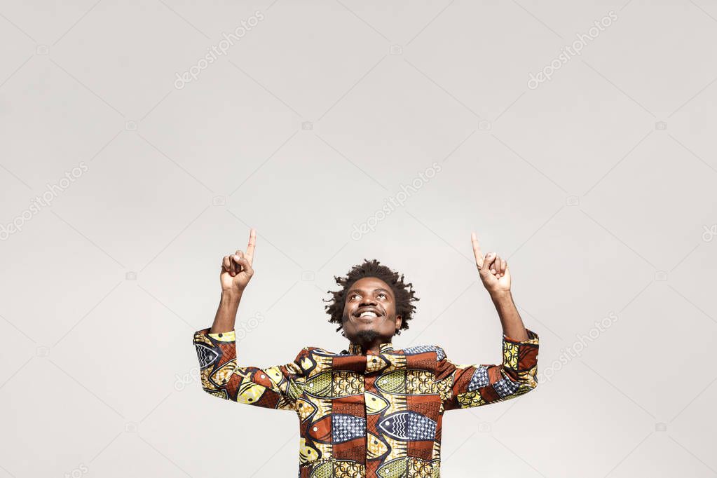 Happiness african man pointing finger up at copy space. Indoor, isolated on gray background