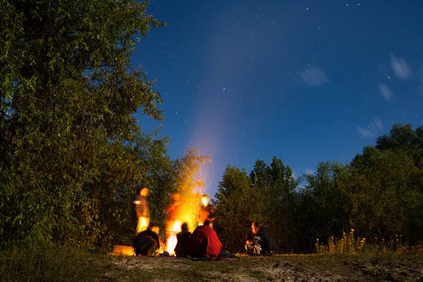 夜に砂浜で大きな明るい焚き火の周りに座って観光客 — ストック写真