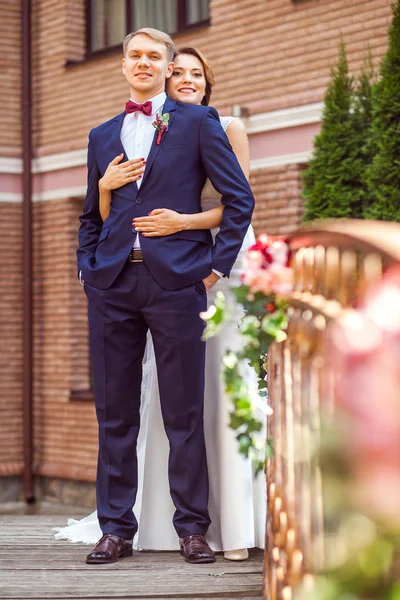 レンガの家の近くの橋の上に立っている間ハグ ハンサムな新郎を魅力的な花嫁 — ストック写真