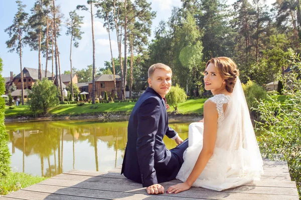 Recém Casados Voltando Olhando Para Câmera Enquanto Sentados Cais Madeira — Fotografia de Stock