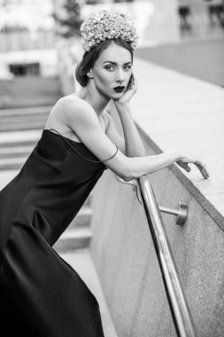 çiçek taç ve metal korkuluk merdiven üzerine eğilerek siyah elbise giyen güzel kadın