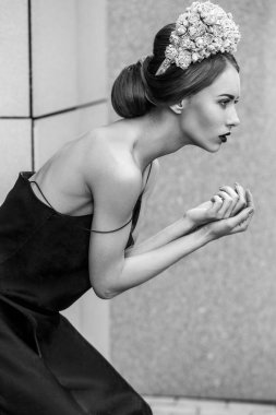 çiçek taç ve poz duvar arka plan üzerinde siyah elbise moda kadın yan görünüm 