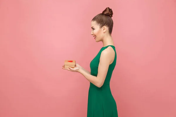 ギフト ボックスを呈した心ピンクの背景に緑のドレスで笑顔の美しい女性の側面図 — ストック写真