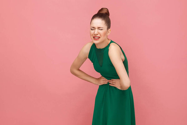 woman bending in half from pain in belly on pink background, stomach pain concept 
